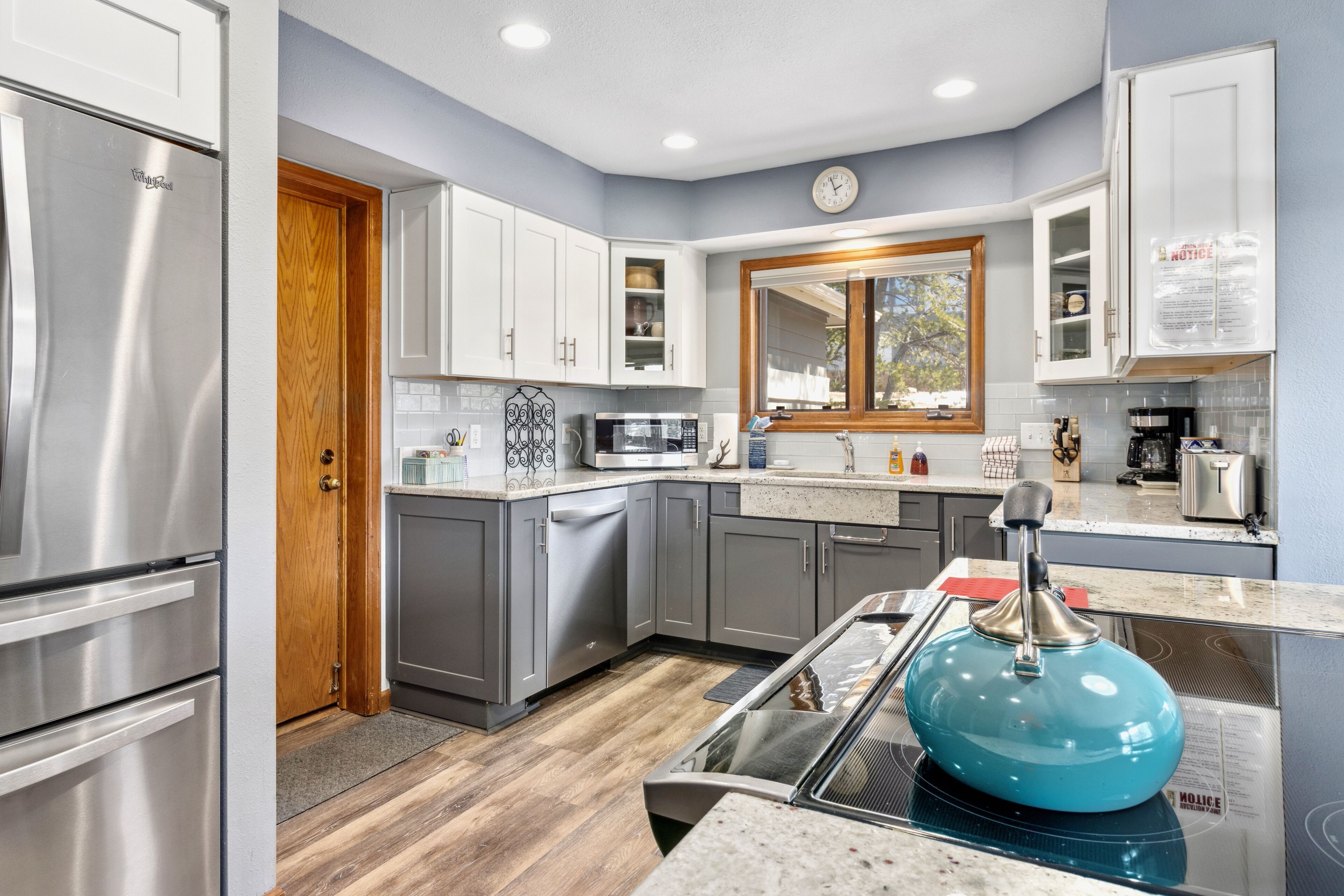 A modern kitchen with stainless steel appliances, grey cabinets, and a wooden door.