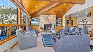 A spacious living room with a stone fireplace, large windows offering mountain views, and a cozy seating area with a sofa and armchairs.