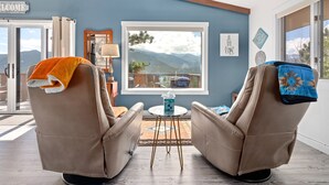 A room with two leather recliners, a small round table, and a view of mountains through a large window. - Divine Destiny Luxury At Windcliff 6 Bedroom Condo by RedAwning (Estes Park)