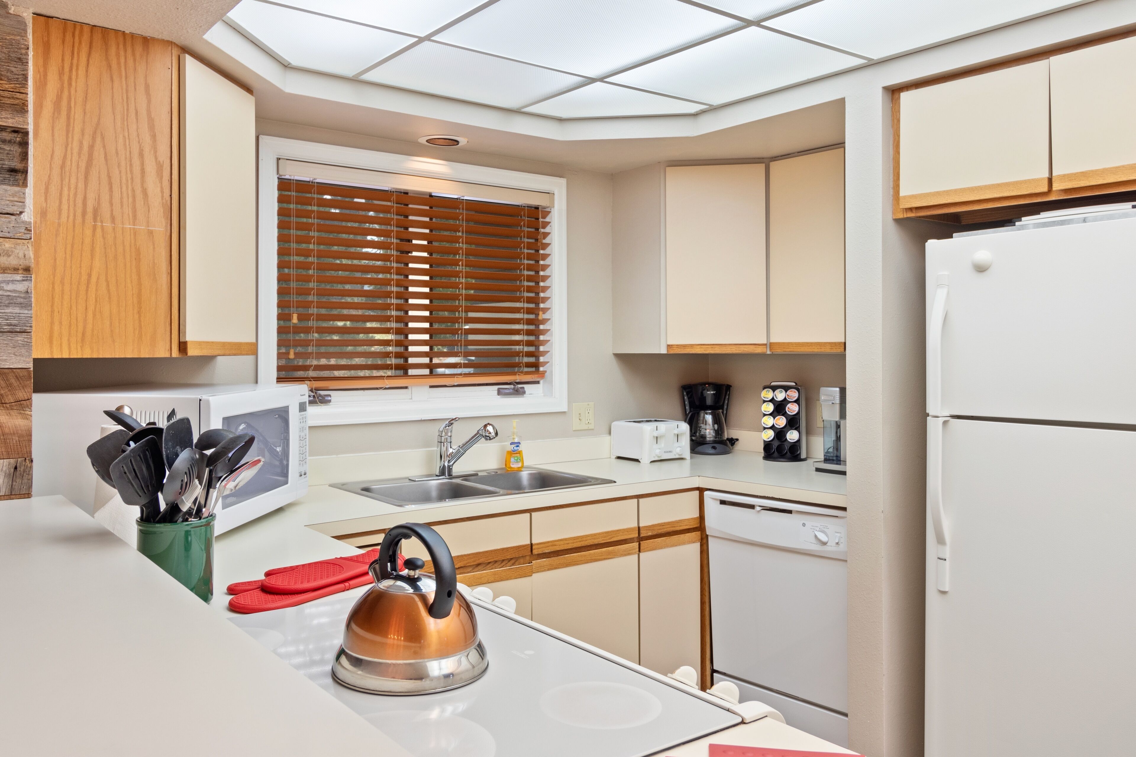 A modern kitchen with wooden cabinets, a stainless steel kettle, a microwave, a sink, and a dishwasher.