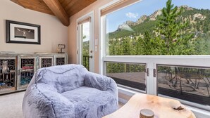 A room with a large window, a plush armchair, a wooden table, and a framed picture on the wall. - Wanderlust Luxury Vacation At Windcliff 3 Bedroom Condo by RedAwning (Estes Park)