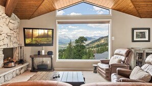 A cozy living room with a stone fireplace, leather sofas, a large TV, and a scenic mountain view through a large window. - Wanderlust Luxury Vacation At Windcliff 3 Bedroom Condo by RedAwning (Estes Park)