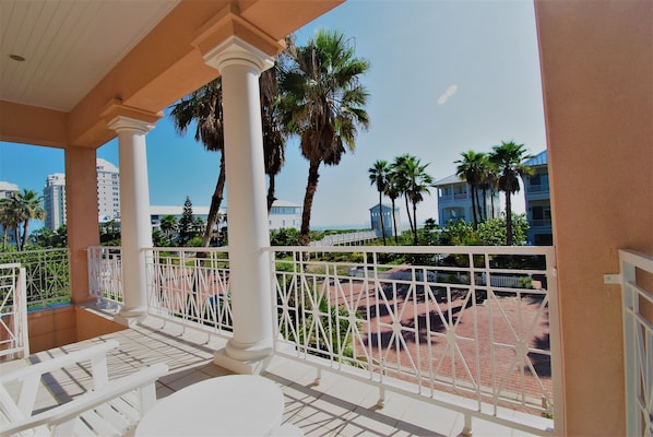 A balcony with white railings, palm trees, and a view of a building complex.