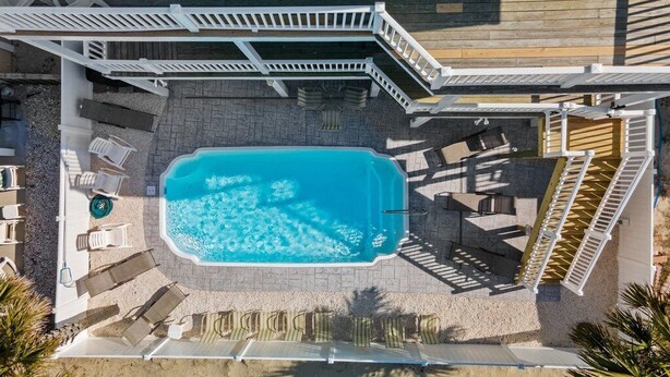 An aerial view of a swimming pool area with a wooden deck, lounge chairs, and a white fence. - Gorgeous 6BR Beach House,OceanViews, Pool, 20 Steps to Beach, 1 PM Check In 2027 (Ocean Isle Beach)