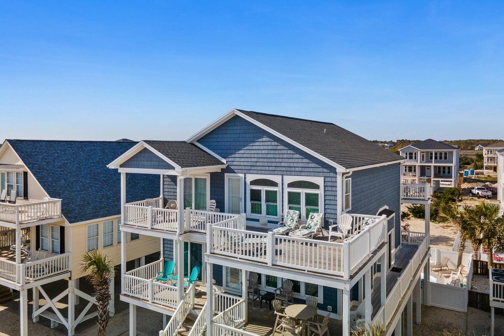 Une propriété en bord de mer, composée de plusieurs étages, dotée de balcons et d’un espace extérieur aménagé pour s’asseoir.