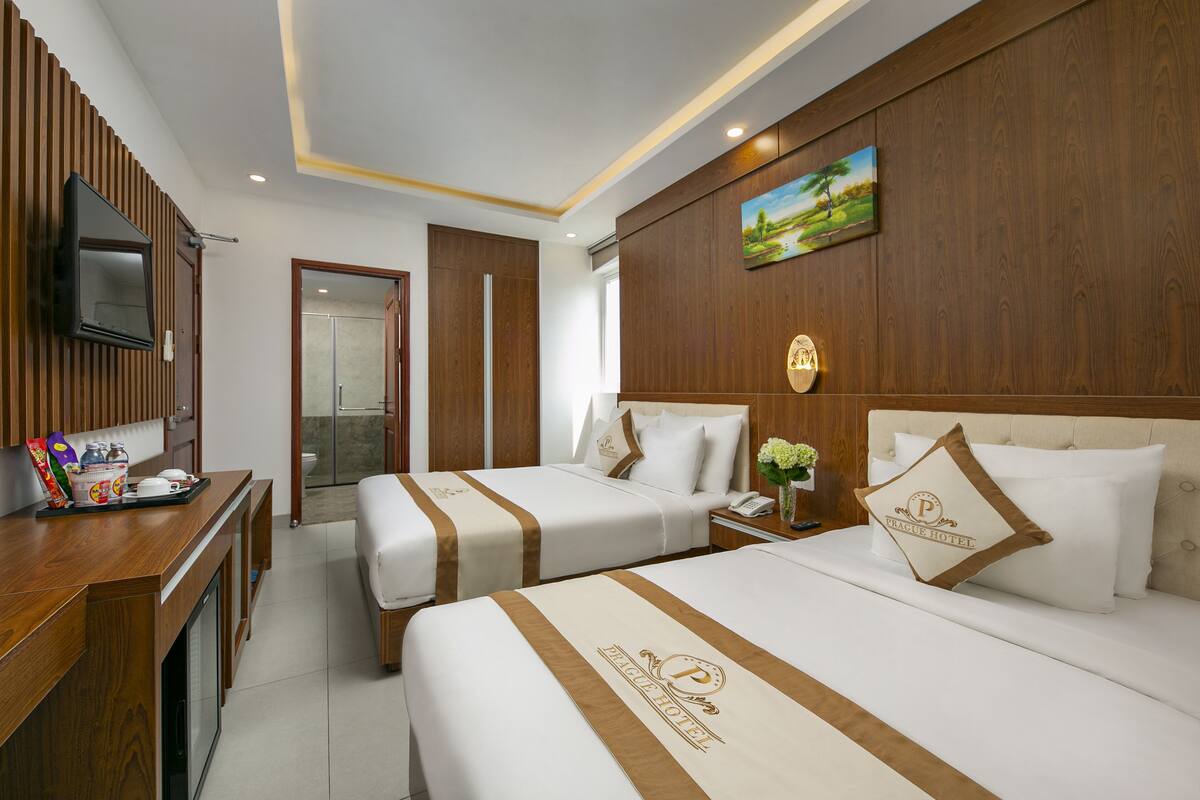 A hotel room with two beds, a wooden desk, a television, and a painting on the wall.