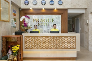 A reception desk at Prague Hotel with a decorative panel, clocks, and a floral arrangement. - Prague Hotel (Da Nang)
