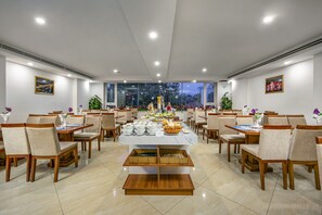 Ein geräumiger Essbereich mit mehreren Tischen und Stühlen, einem Buffet und großen Fenstern mit Blick ins Freie.
