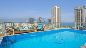 A rooftop pool with lounge chairs and a view of a city skyline. - Prague Hotel (Da Nang)