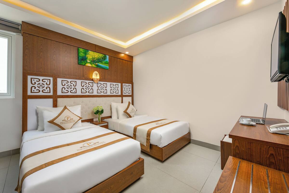 A hotel room with two beds, a desk, a TV, and a wall with decorative panels.