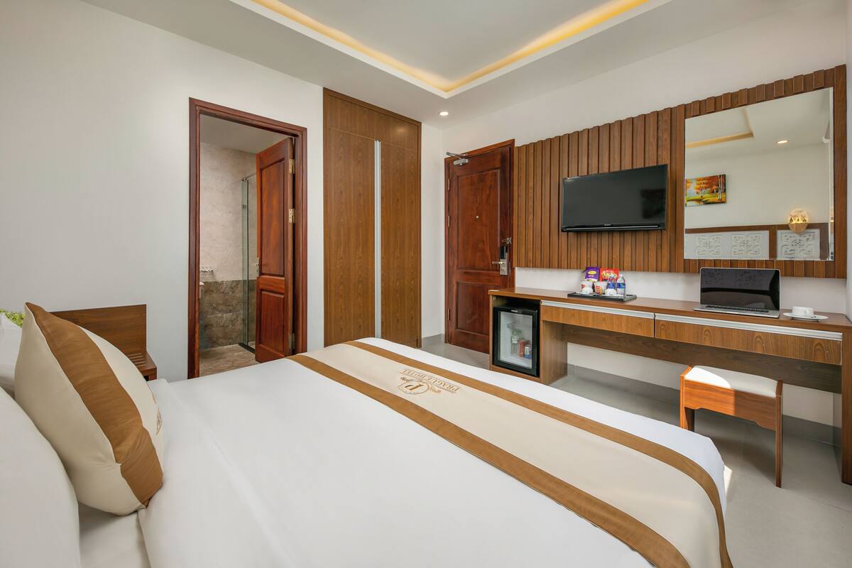 A hotel room with a bed, a desk with a computer, a television, and a small refrigerator.