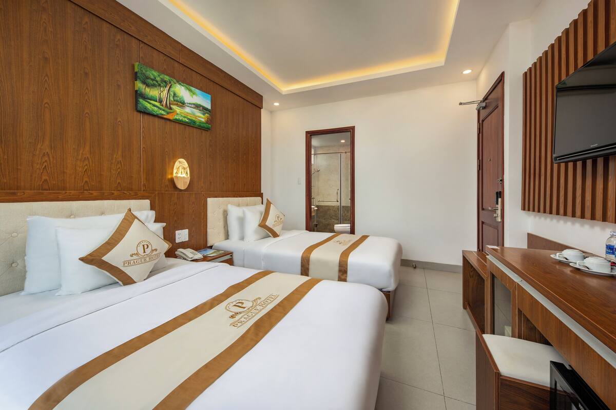 A hotel room with two beds, a wooden headboard, a painting, a TV, and a desk with a cup and saucer.