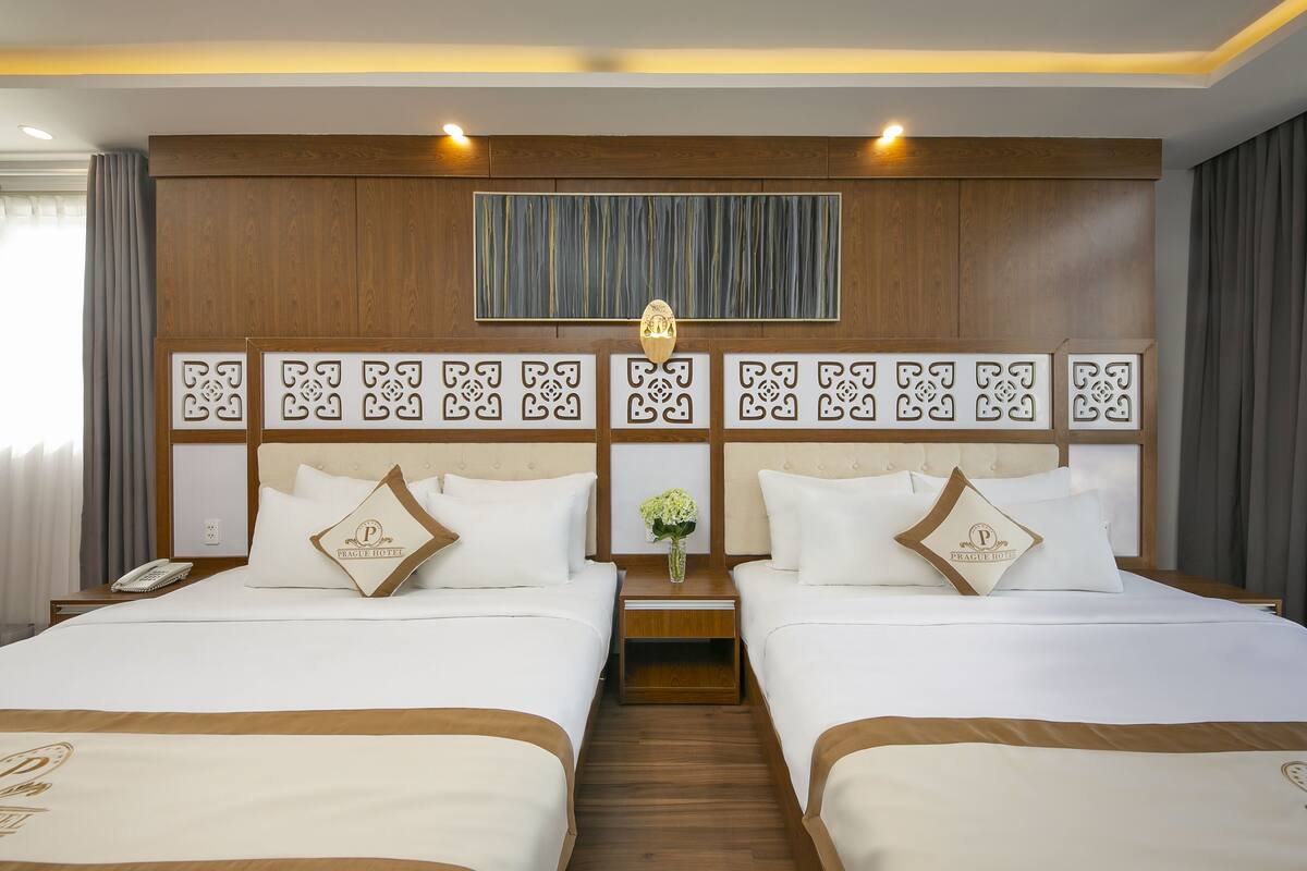 A hotel room with two beds, a wooden headboard, a nightstand with a phone, and a decorative wall panel.