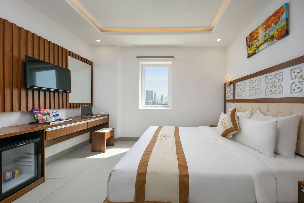 A hotel room with a bed, a desk with a computer, a television, and a window with a city view.