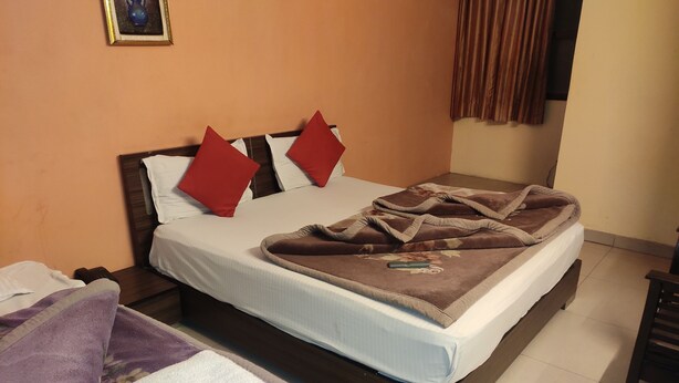 A neatly made bed with a brown blanket and red pillows, a purple towel, and a small framed picture on the wall. - Hotel Trio Tourist (New Delhi)