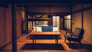 A traditional Japanese room with tatami flooring, a low wooden table, a sofa with cushions, and a chair.