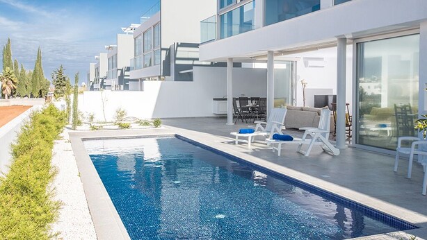 Uma área moderna na piscina com uma piscina retangular, cadeiras de lounge brancas e um espaço de refeições com móveis de exterior.