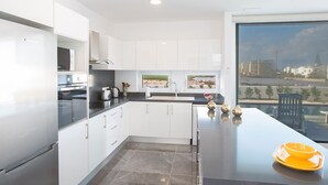 Uma cozinha moderna com armários brancos, bancada preta e vista para a cidade através de grandes janelas.