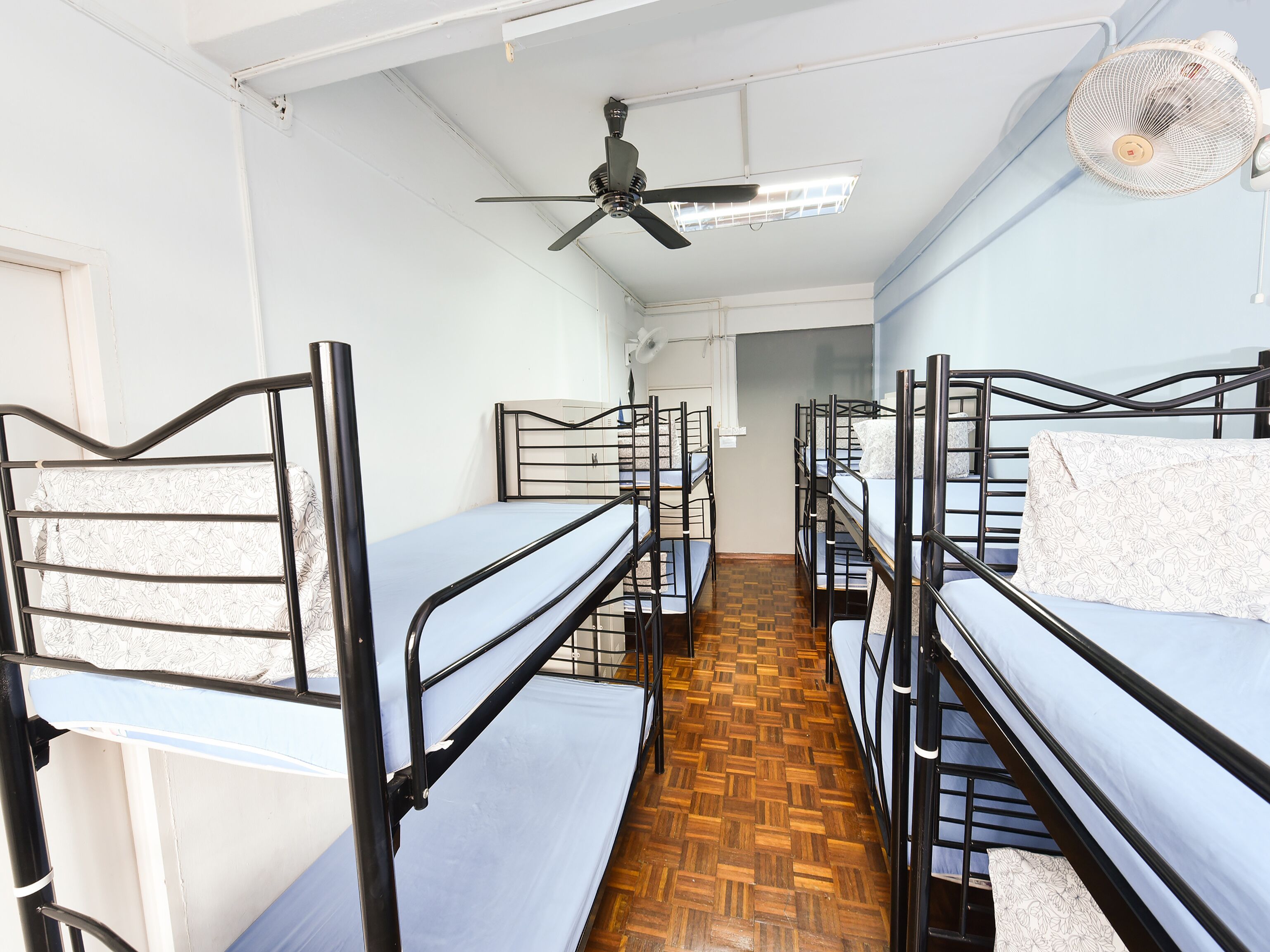 A dormitory room with bunk beds, a ceiling fan, and a wooden floor.