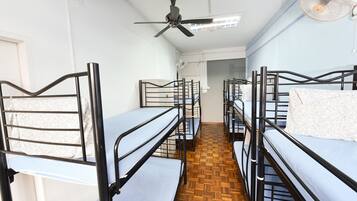 A dormitory room with bunk beds, a ceiling fan, and a wooden floor.