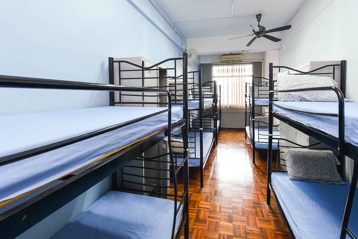 A dormitory room with bunk beds, a ceiling fan, and a window with blinds.