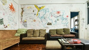 A room with a wooden herringbone floor, two sofas, a small ottoman, and a cluttered coffee table. The walls are covered with various writings and drawings. - Hotel O Kuantan Backpackers (Kuantan)