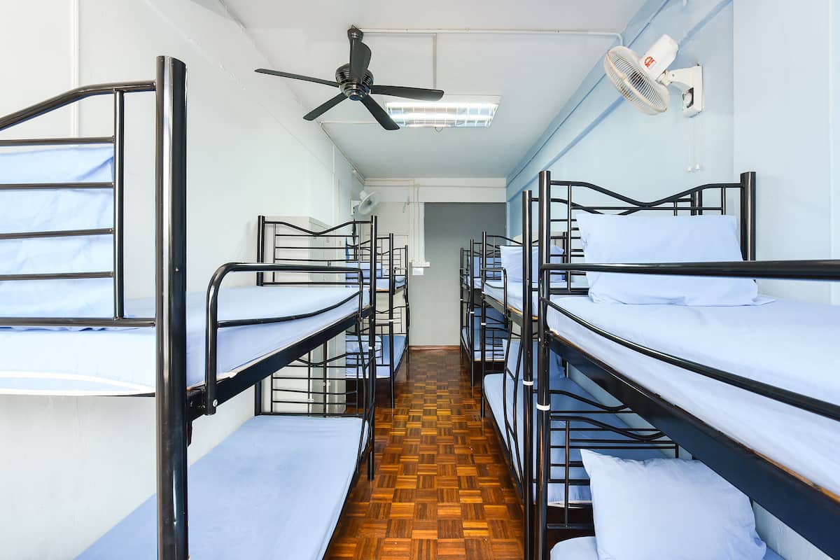 A dormitory room with bunk beds, a ceiling fan, and a wall-mounted heater.