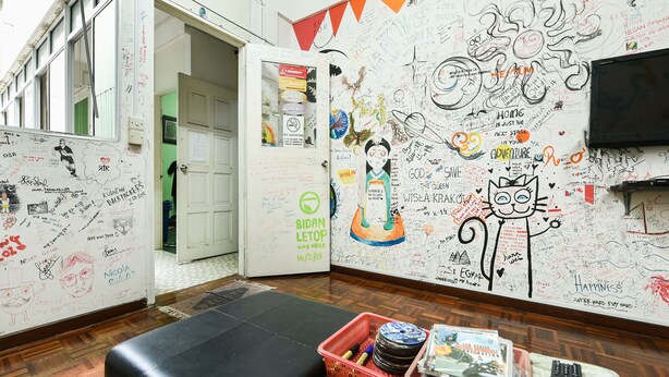 A room with a whiteboard covered in various writings and drawings, a black leather ottoman, and a table with books and a remote control. - Hotel O Kuantan Backpackers (Kuantan)