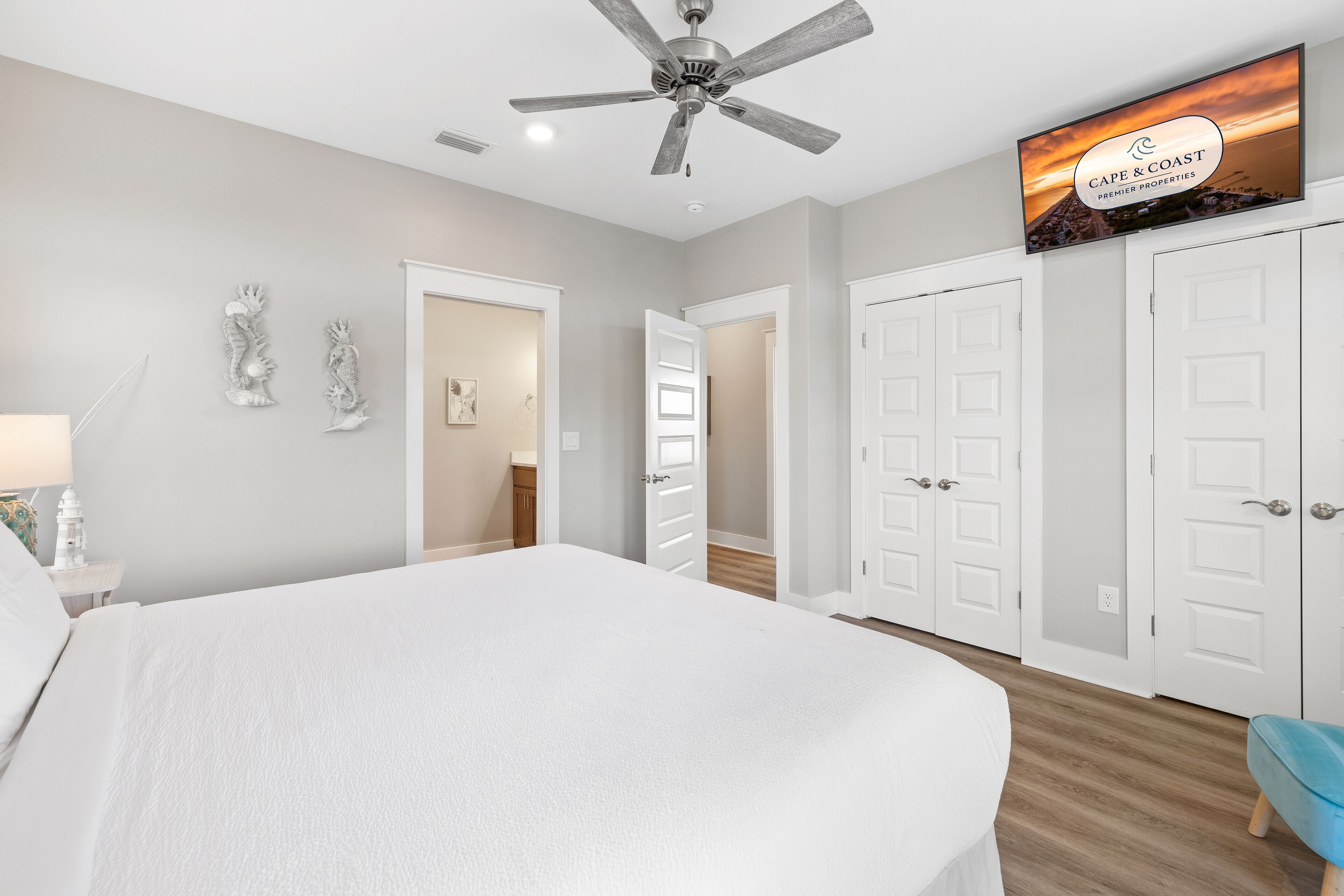 A bedroom with a large bed, a ceiling fan, a TV mounted on the wall, and white doors.