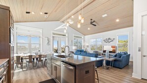 Una cocina amplia con una isla central, un comedor con sillas y una sala de estar con sofá y mesa de centro.