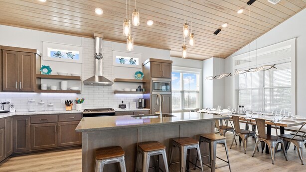 Cocina moderna con alacenas de madera, una isla central con taburetes, electrodomésticos de acero inoxidable e iluminación colgante.