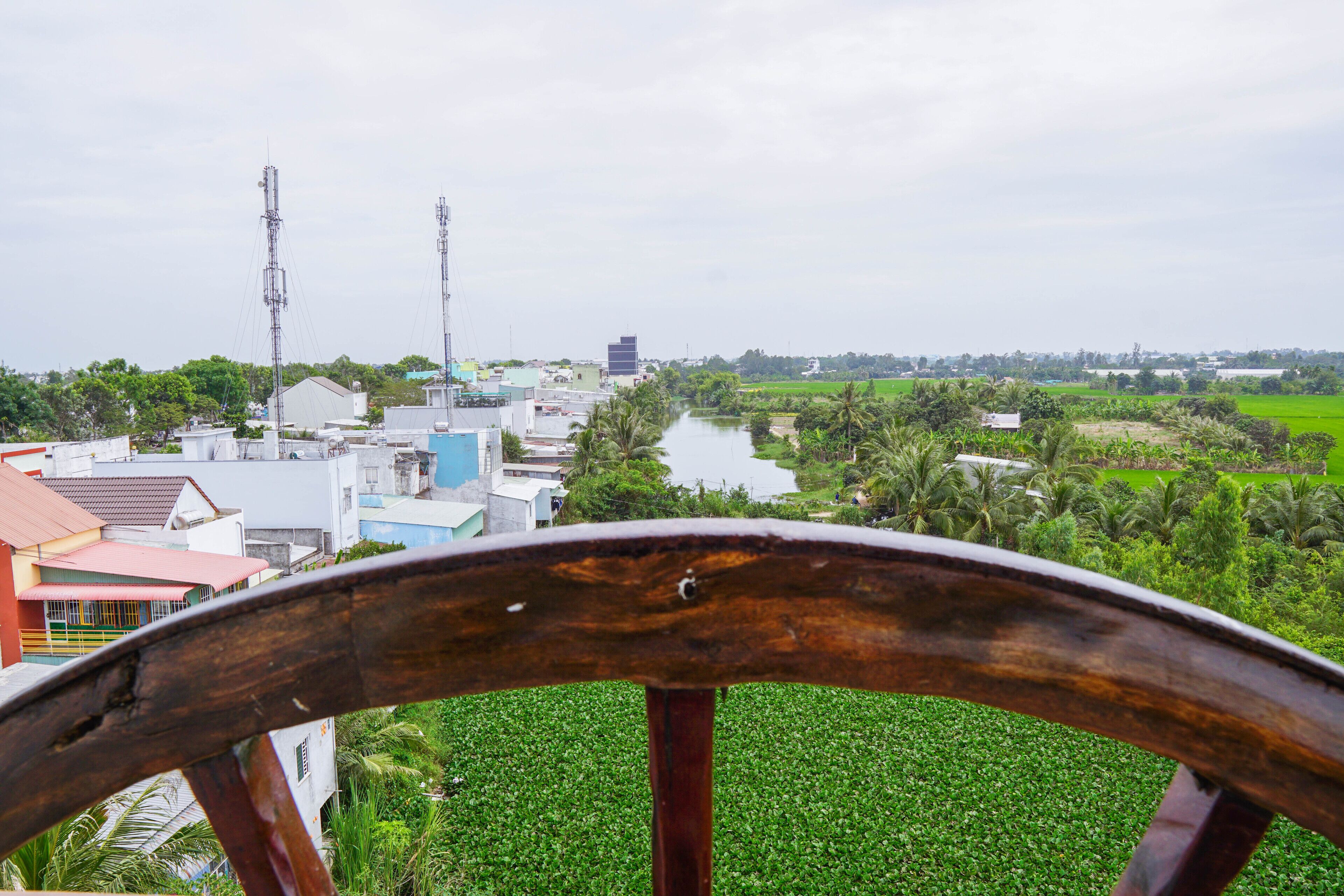 A view from a wooden structure overlooking a town with buildings, a river, and green fields.
