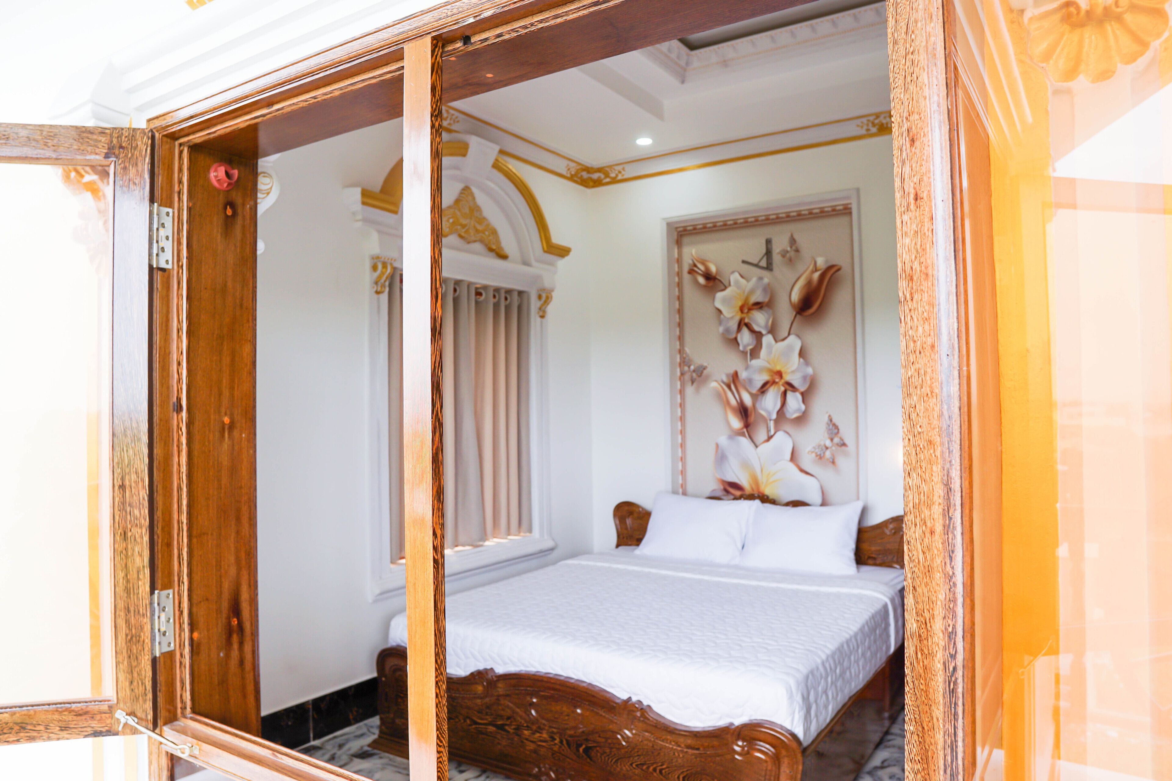 Una habitación con una cama de madera, ropa de cama blanca, un adorno en la pared y una ventana con cortinas.