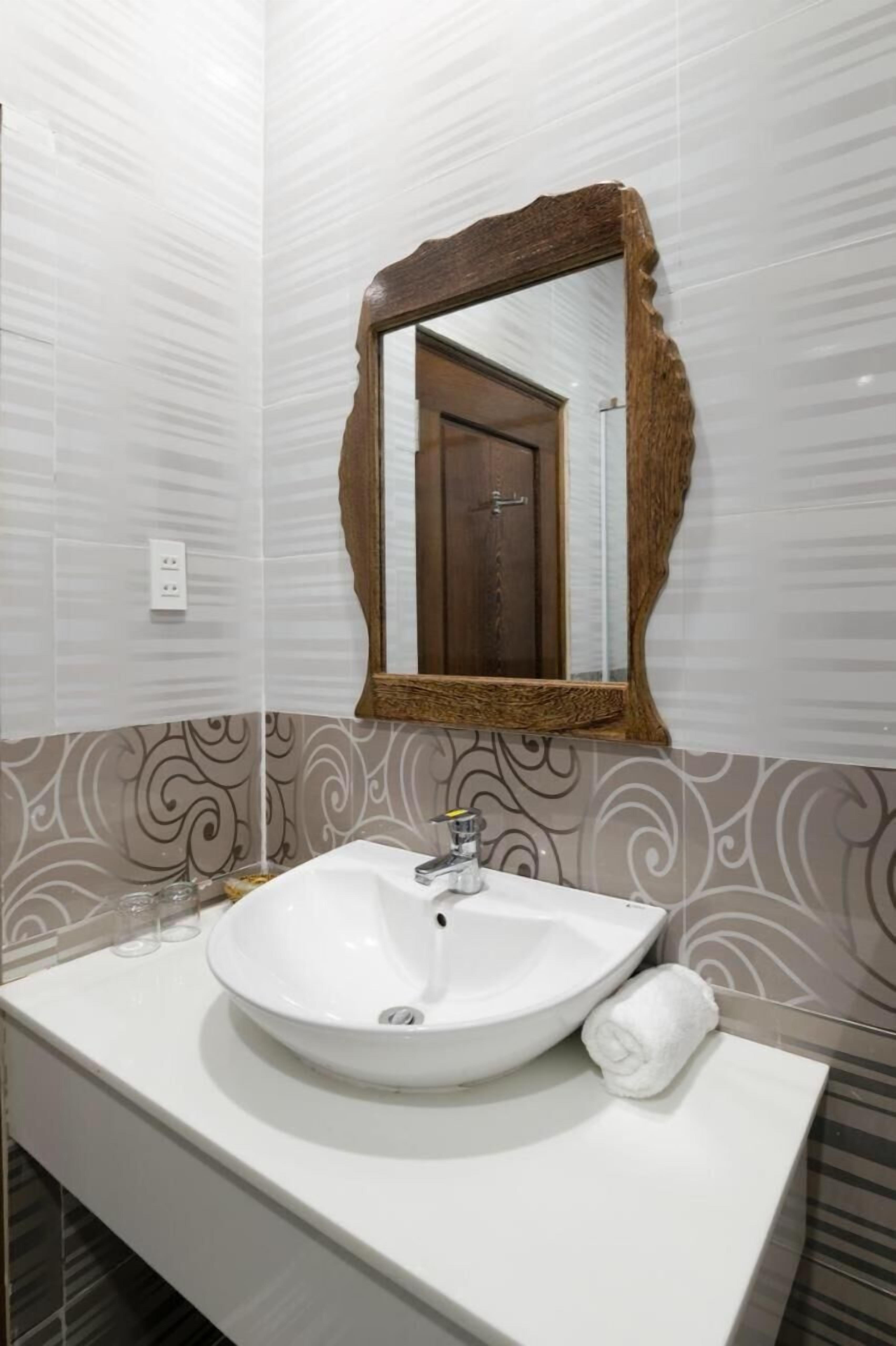 Un baño con lavamanos blanco, un espejo con marco de madera y papel tapiz estampado.