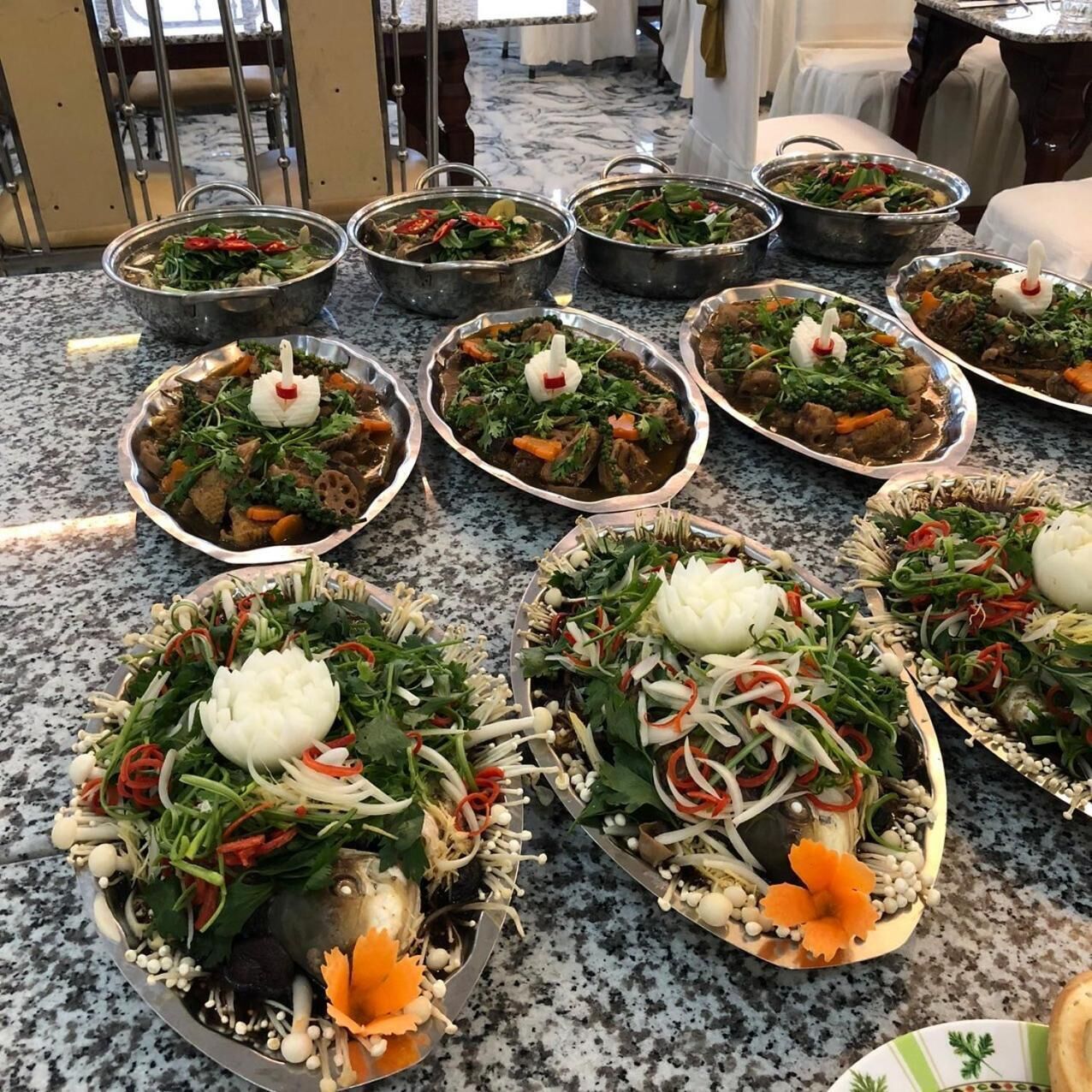 A variety of dishes arranged on a marble table in a dining area with chairs and a view of the room.