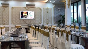 Uma sala de jantar formal com uma mesa comprida, cadeiras brancas com fitas douradas e um candelabro.