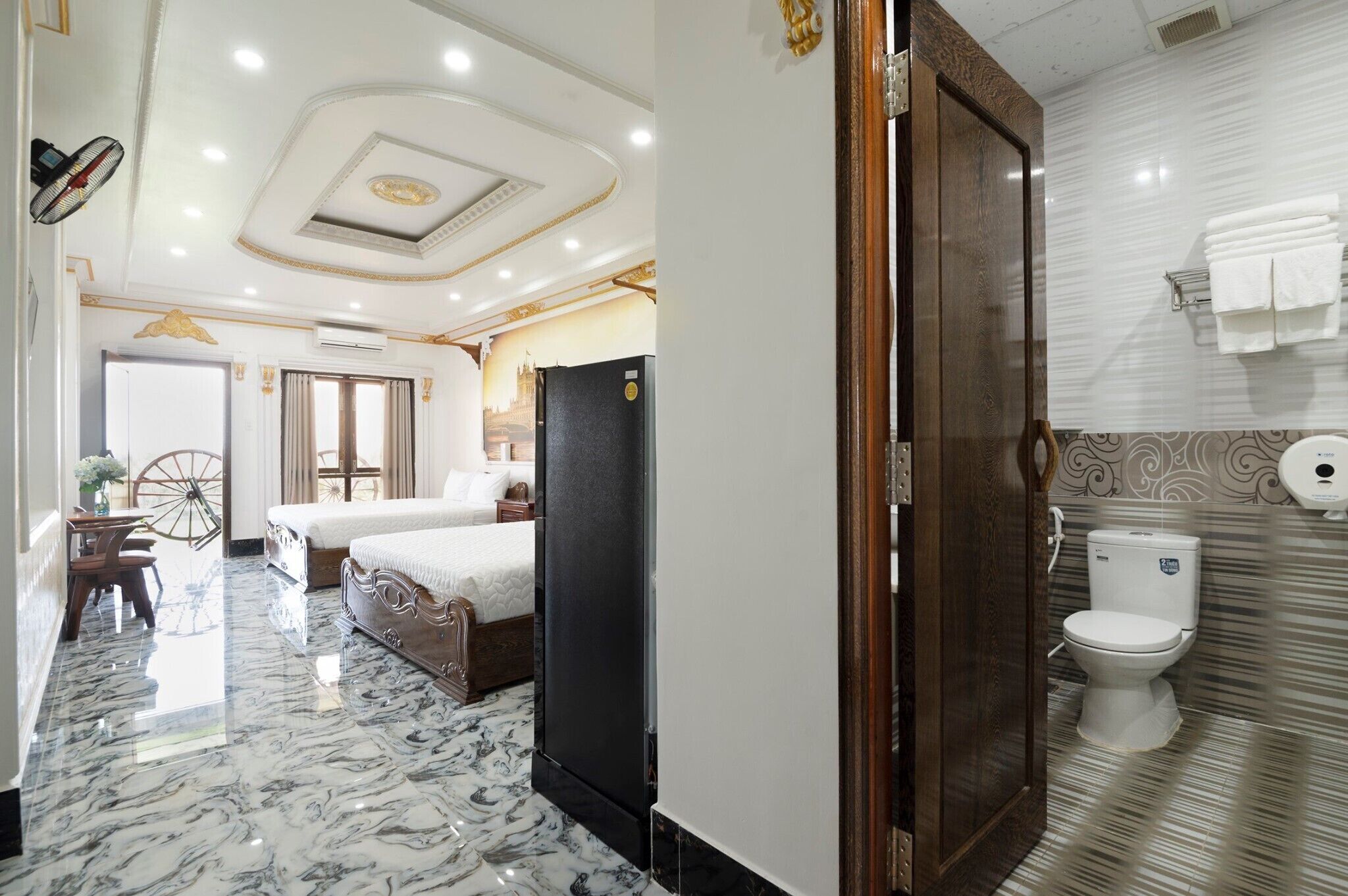Une chambre d’hôtel équipée d’un lit, d’un réfrigérateur, d’une porte en bois et d’une salle de bain avec des toilettes et un porte-serviettes.