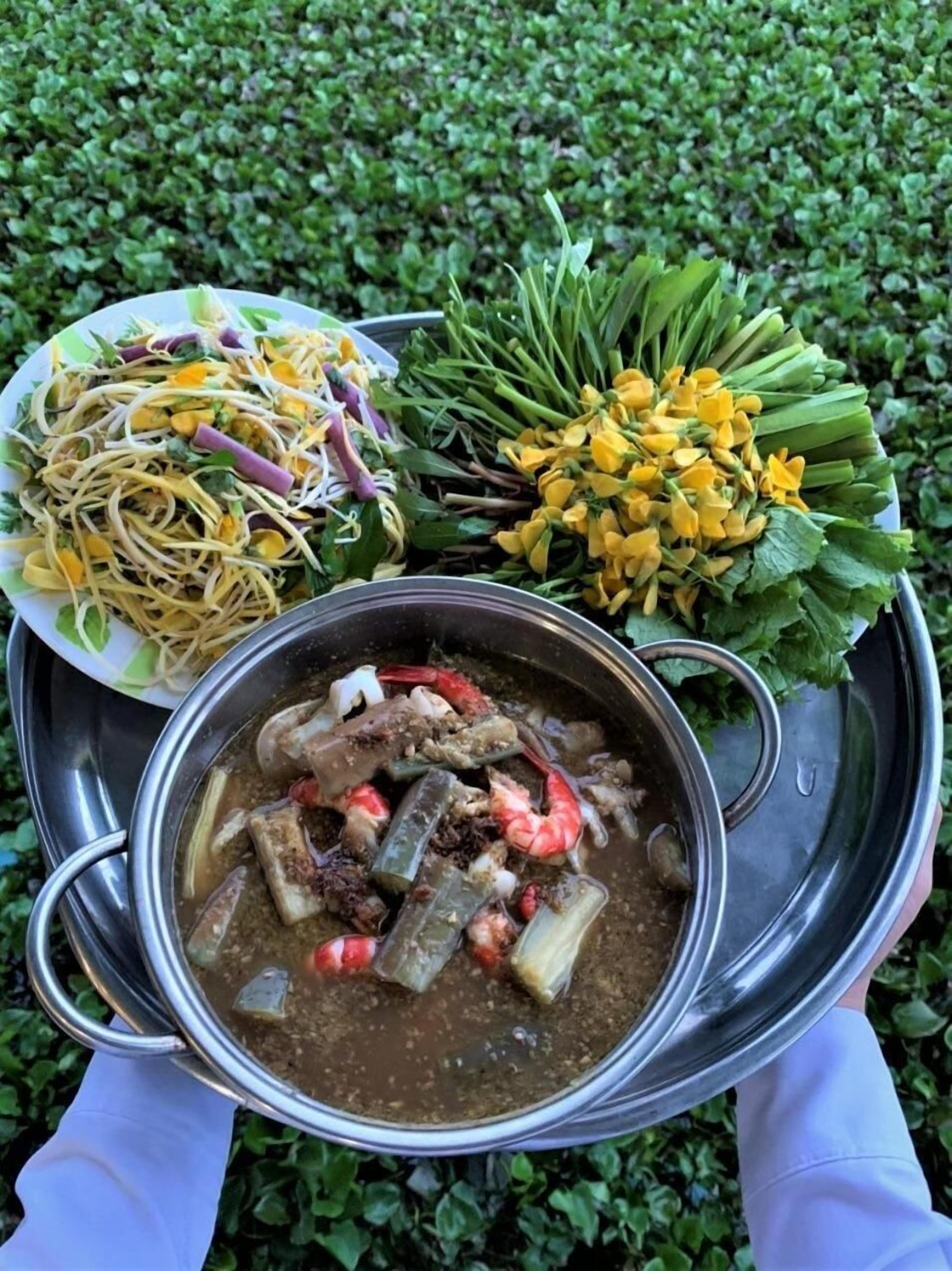 A tray with a bowl of soup, a plate of noodles, and a bunch of yellow flowers.