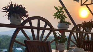 Mesa de madeira com cadeiras e plantas em vasos numa varanda com vista panorâmica.