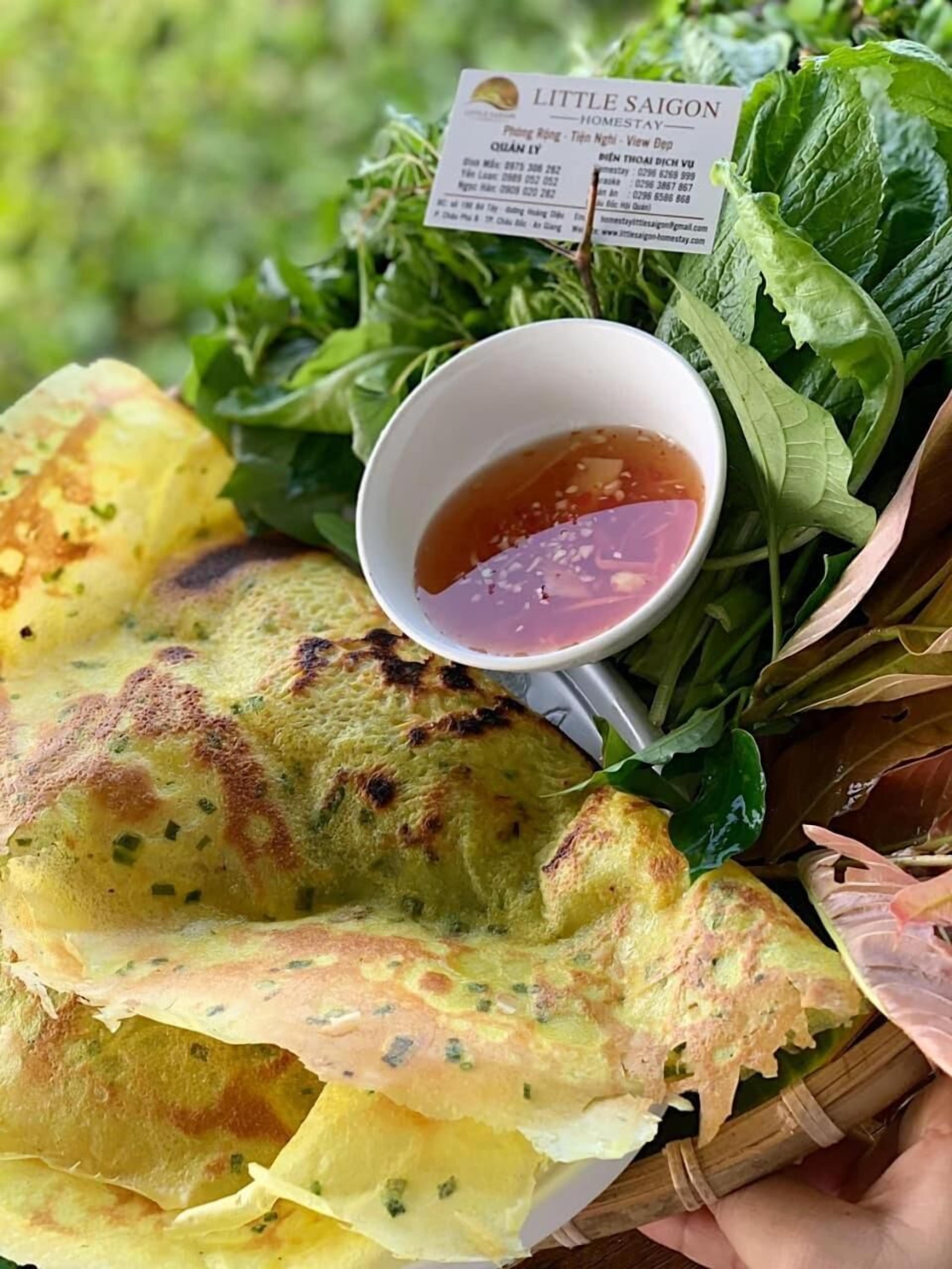 A basket containing a grilled pancake, fresh herbs, and a small bowl of dipping sauce.