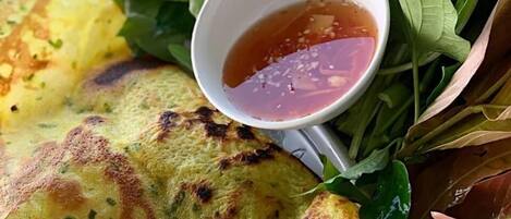 A basket containing a grilled pancake, fresh herbs, and a small bowl of dipping sauce.