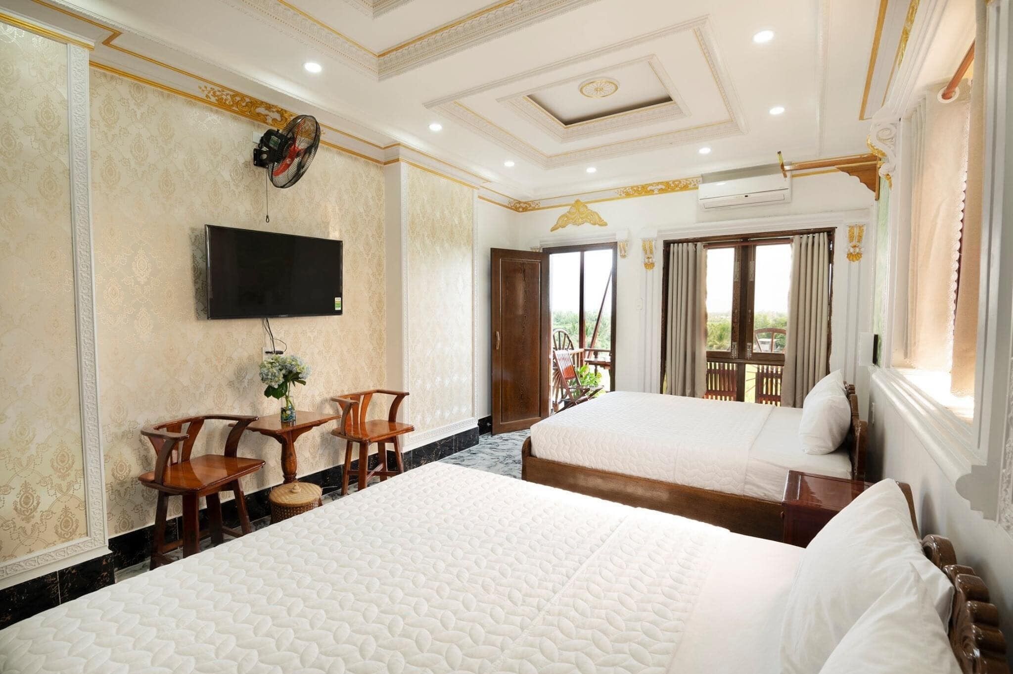 Habitación de hotel con dos camas, televisión, ventilador y balcón con cortinas.