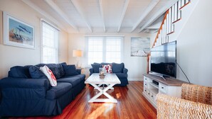 A living room with two dark blue sofas, a white coffee table, a TV on a wooden stand, and a staircase with wooden railings.