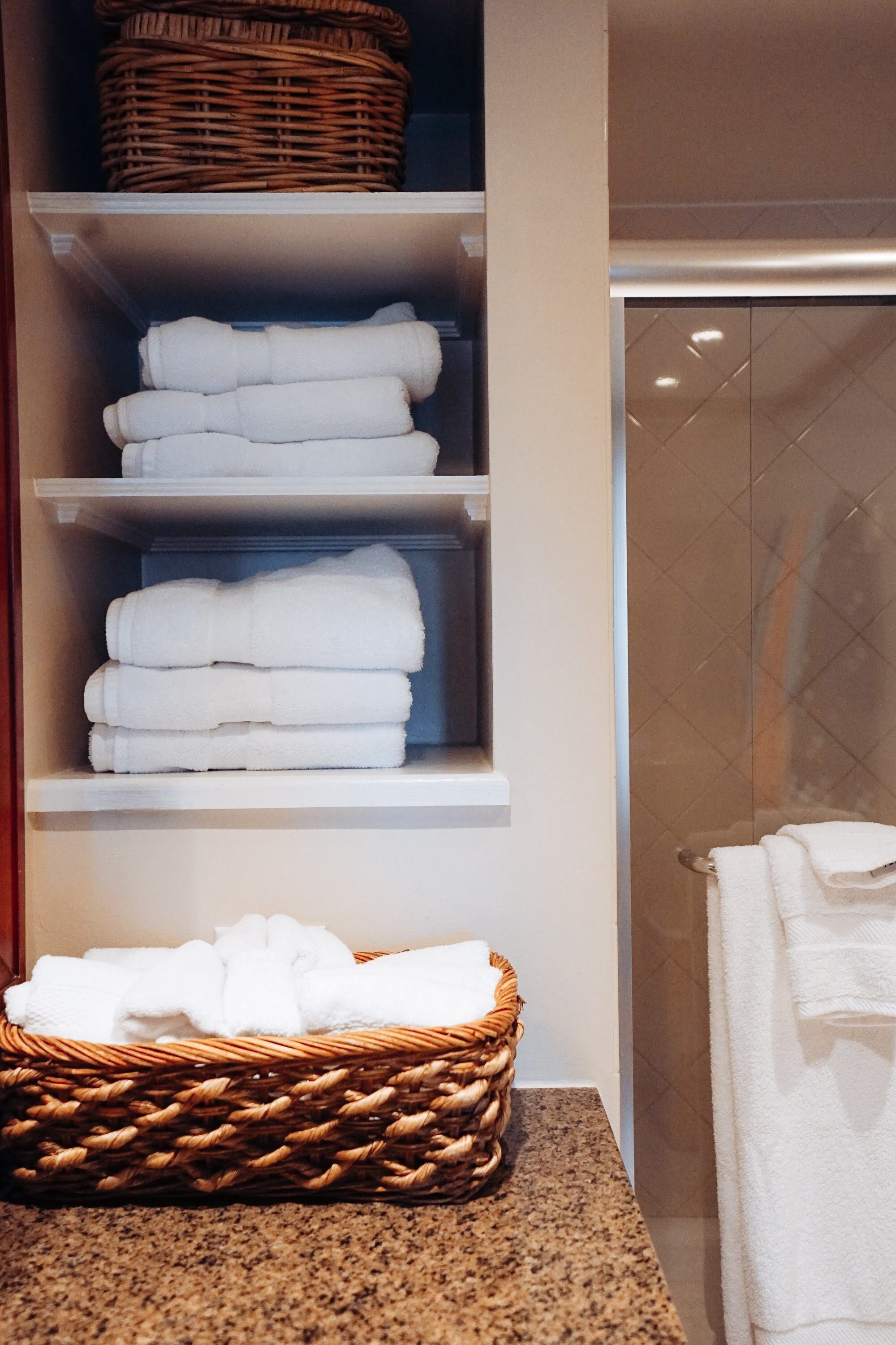 A bathroom with a towel rack, a wicker basket, and a shelf with folded towels.