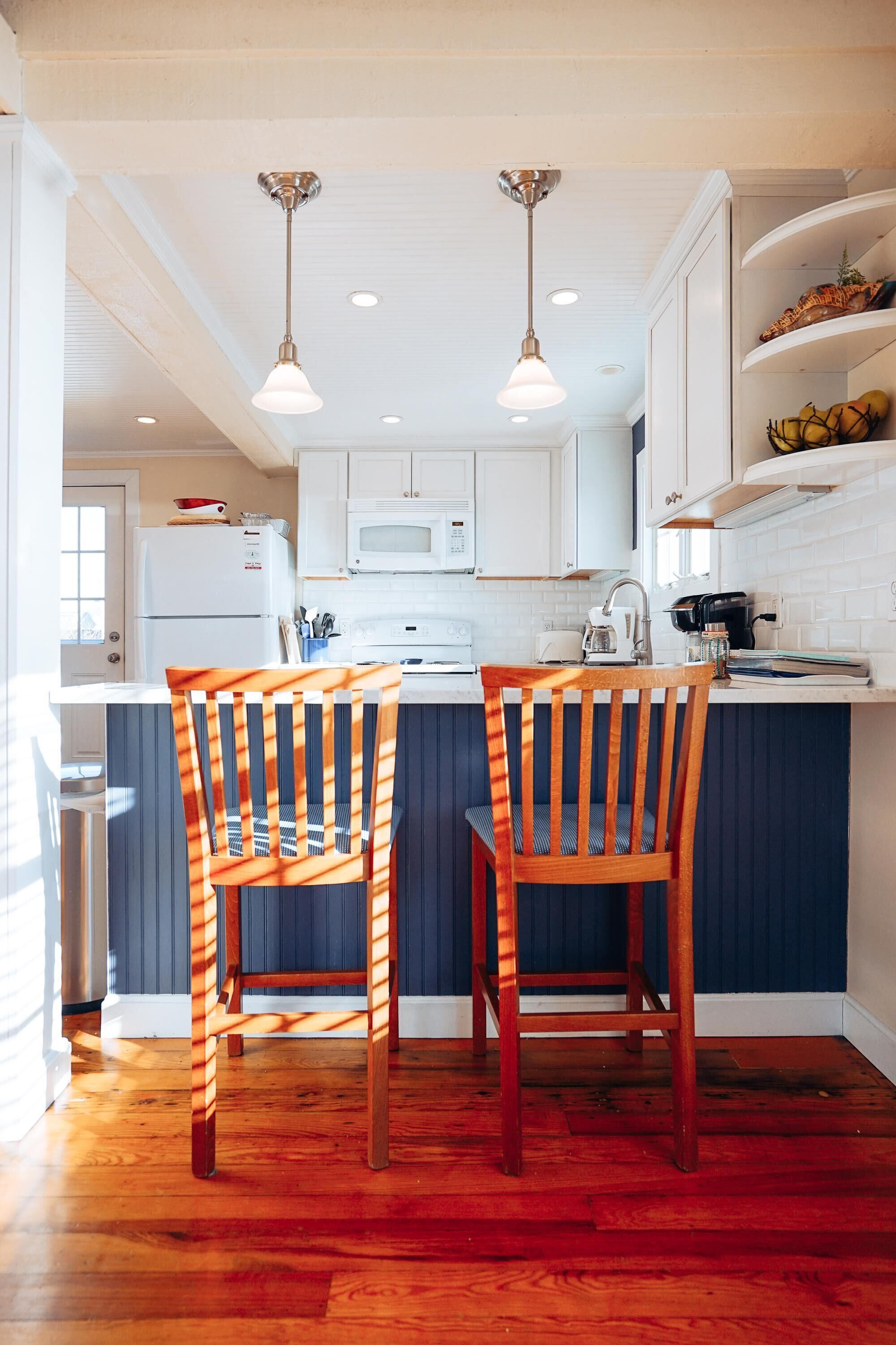 A kitchen with white cabinets, a blue island, two wooden chairs, and pendant lights.