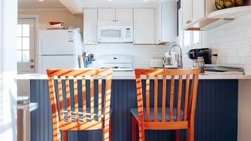 A kitchen with white cabinets, a blue island, two wooden chairs, and pendant lights.