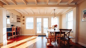 A spacious kitchen with wooden floors, a dining area with a table and chairs, and a view through the glass doors.