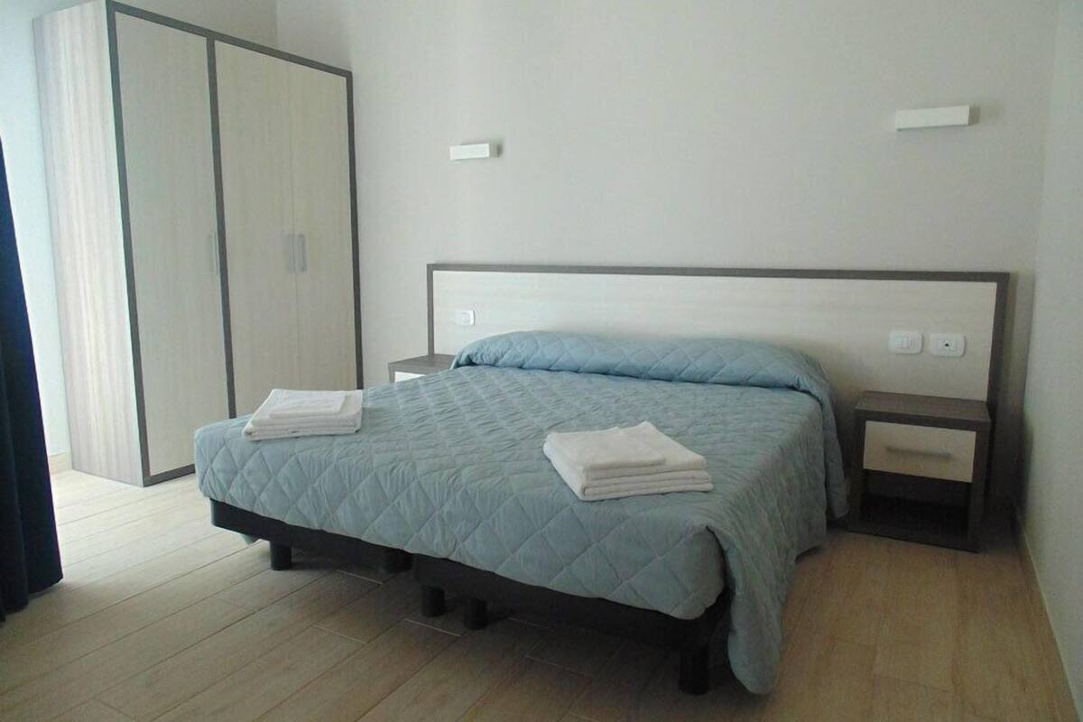 A bedroom with a bed, two bedside tables, a wardrobe, and a nightstand.
