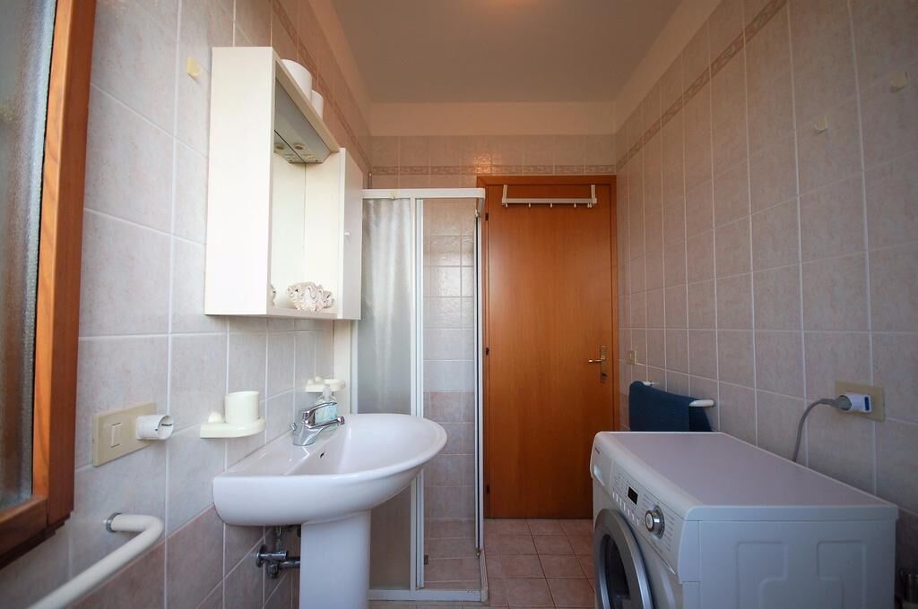 A compact bathroom with a sink, mirror, towel rack, shower, and a washing machine.