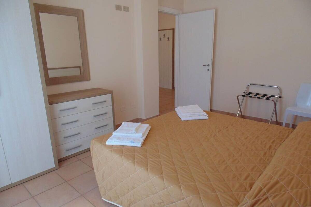 A bedroom with a bed, a dresser, a mirror, a door, and a chair.